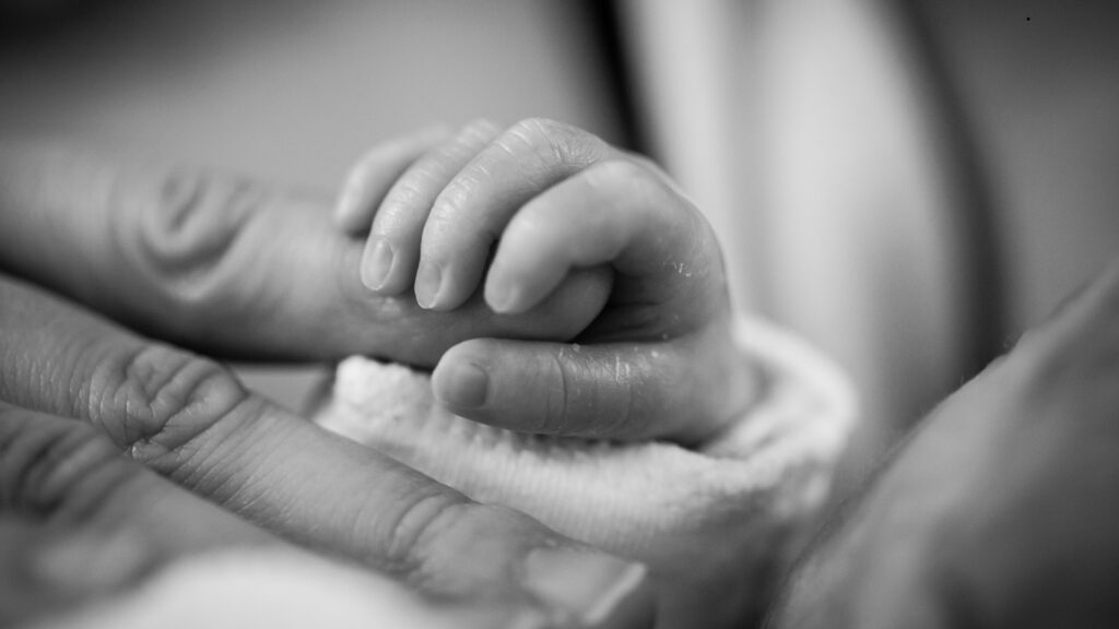 An AI generated image of an adult holding the hands of a new-born, depicting automatic citizenship by birth
